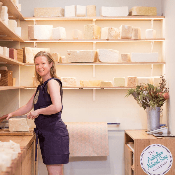 ANSC 創辦人 Emma 在恆溫熟成室中親自切開熟成手工皂。背景可見整齊排列、正處於 4 至 6 週自然熟成期的皂餅，展現冷製法工藝對時間與品質的堅持。