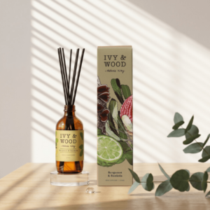 IVY&WOOD佛手柑與澳洲忍冬擴香瓶商品主圖，琥珀色玻璃瓶擺放在透明水晶底座，旁有滿版植物插畫包裝盒與尤加利葉，牆面呈現百葉窗自然晨光光影