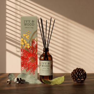 IVY & WOOD 原野精靈擴香瓶居家生活美學情境。全新插畫外盒與琥珀精油瓶身放置於純淨牆面前，右側投射出明亮乾淨的百葉窗斜射陽光樹影，完美將澳洲原生森林的通透與平靜感帶入現代城市公寓中。