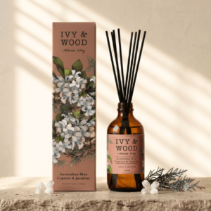 IVY & WOOD 澳洲藍絲柏與茉莉室內擴香瓶，煙燻粉橘插畫外盒與琥珀玻璃瓶身在斜射陽光百葉窗光影下的高奢陳列