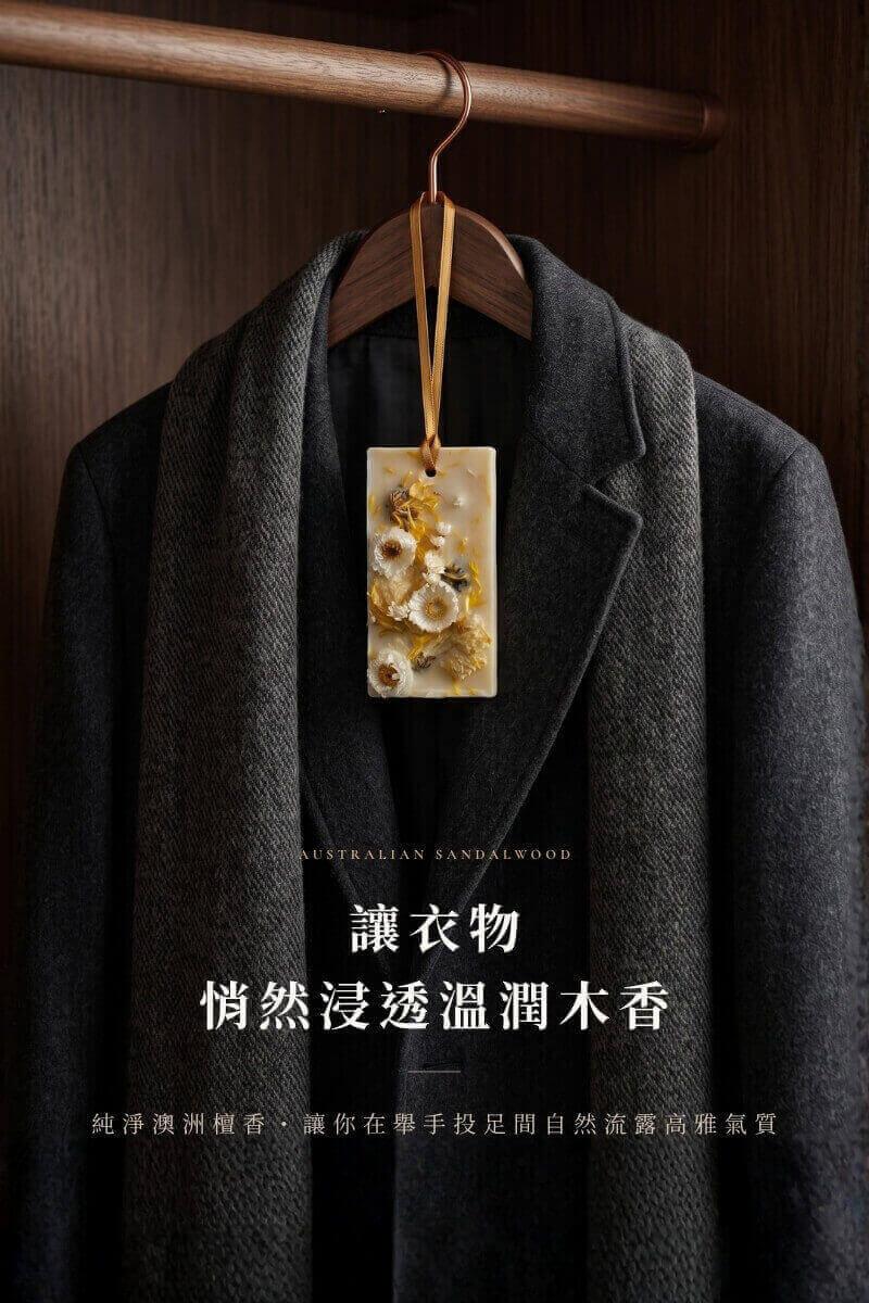 純淨澳洲檀香精油蠟牌懸掛於深灰毛呢西裝大衣衣架上，自然浸透衣物纖維，散發不著痕跡的高尚從容品味